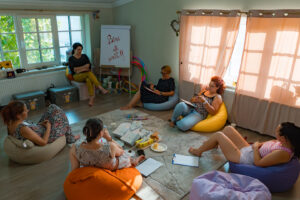 Grup de femei participante la Șezătoarea urbană MindCocktail, într-un spațiu cald și intim, stând relaxate și împărtășind povești, aflând informații utile