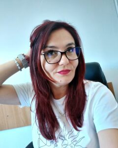 Portret al Elvirei purtând ochelari de vedere și trecându-și mâna prin păr, cu un zâmbet discret și o atitudine jucăușă, pregătită pentru Spring SuperBlog 2026.Titlu: Elvira – Autenticitate și joacă în cuvinte la SuperBlog.